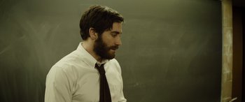 Movie still from “Enemy” (2013), directed by Denis Villeneuve – A man with a beard wearing a white shirt and a tie; Medium shot, Over the shoulder angle