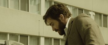 Movie still from “Enemy” (2013), directed by Denis Villeneuve – A man in a suit looking to his left; Close Up shot, Low angle