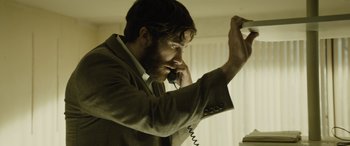 Movie still from “Enemy” (2013), directed by Denis Villeneuve – A man talking on a phone while holding a phone to his ear; Close Up shot, Low angle