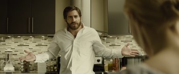 Movie still from “Enemy” (2013), directed by Denis Villeneuve – A man in a white dress shirt is in a kitchen; Medium shot, Over the shoulder angle
