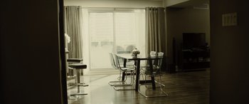 Movie still from “Enemy” (2013), directed by Denis Villeneuve – A dining room table and chairs in front of a sliding glass door; Wide shot, High angle