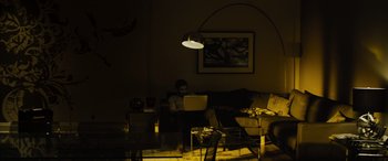 Movie still from “Enemy” (2013), directed by Denis Villeneuve – A man sitting on a couch using a laptop; Wide shot, High angle