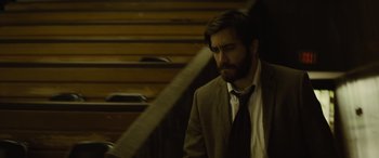 Movie still from “Enemy” (2013), directed by Denis Villeneuve – A man wearing a suit and tie standing next to a staircase; Close Up shot, Low angle