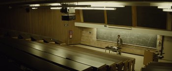 Movie still from “Enemy” (2013), directed by Denis Villeneuve – A man standing in front of a chalkboard in a classroom; Wide shot, High angle