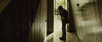 Movie still from “Enemy” (2013), directed by Denis Villeneuve – A man standing in front of a door and a window; Wide shot, Low angle
