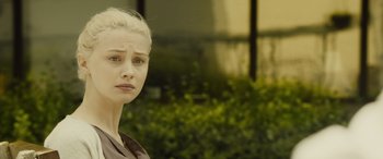 Movie still from “Enemy” (2013), directed by Denis Villeneuve – A young woman with blonde hair is standing in front of a building; Close Up shot, Over the shoulder angle