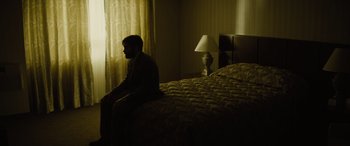 Movie still from “Enemy” (2013), directed by Denis Villeneuve – A man sitting on the edge of a bed in a bedroom; Wide shot, High angle