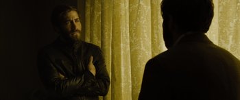 Movie still from “Enemy” (2013), directed by Denis Villeneuve – A man standing next to another man in front of a curtain; Medium shot, Over the shoulder angle