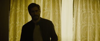 Movie still from “Enemy” (2013), directed by Denis Villeneuve – A man standing in front of a window with curtains; Medium shot, Low angle