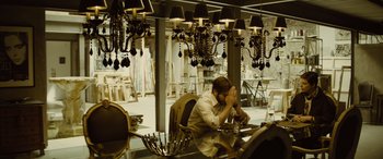 Movie still from “Enemy” (2013), directed by Denis Villeneuve – A man sitting at a table in front of chandeliers; Wide shot, High angle