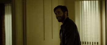 Movie still from “Enemy” (2013), directed by Denis Villeneuve – A man with a goatee smiling for the camera; Medium shot, Over the shoulder angle