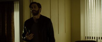 Movie still from “Enemy” (2013), directed by Denis Villeneuve – A man standing in a room with his hand on his chest; Medium shot, Low angle