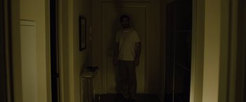 Movie still from “Enemy” (2013), directed by Denis Villeneuve – A man standing in front of a door in a dark room; Wide shot, High angle
