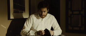 Movie still from “Enemy” (2013), directed by Denis Villeneuve – A man sitting at a table looking down at his cell phone; Medium shot, Over the shoulder angle