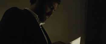 Movie still from “Enemy” (2013), directed by Denis Villeneuve – A man wearing a suit and tie looking at a tablet; Close Up shot, Low angle