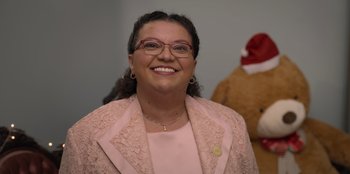 Movie still from “Christmas Full of Grace” (2022), directed by Pedro Antônio Paes – A woman wearing a pink suit and glasses; Close Up shot, Over the shoulder angle