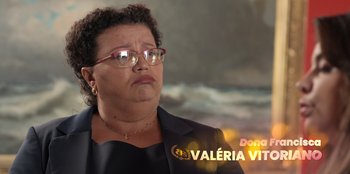 Movie still from “Christmas Full of Grace” (2022), directed by Pedro Antônio Paes – A woman in glasses and a black jacket is in front of a painting; Close Up shot, Low angle