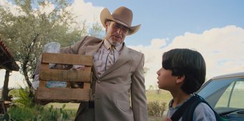 Movie still from “Chupa” (2023), directed by Jonás Cuarón – An older man wearing a suit and a cowboy hat holding a crate; Medium shot, Over the shoulder angle