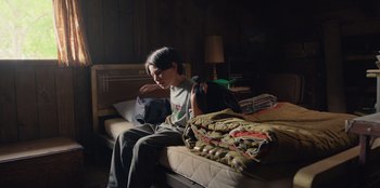 Movie still from “Chupa” (2023), directed by Jonás Cuarón – A person sitting on a bed with a blanket; Medium shot, High angle