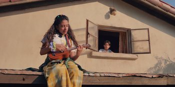 Movie still from “Chupa” (2023), directed by Jonás Cuarón – A young girl is playing a ukulele while a young boy watches from a window; Medium shot, Low angle