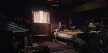 Movie still from “Chupa” (2023), directed by Jonás Cuarón – A person sitting on a bed in a room; Wide shot, High angle