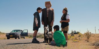 Movie still from “Chupa” (2023), directed by Jonás Cuarón – A group of people standing next to each other on a dirt road; Wide shot, Low angle