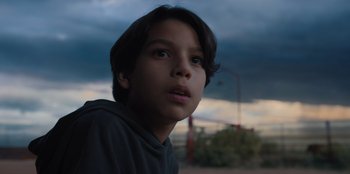 Movie still from “Chupa” (2023), directed by Jonás Cuarón – A young boy looking into the distance with a cloudy sky in the background; Close Up shot, Low angle