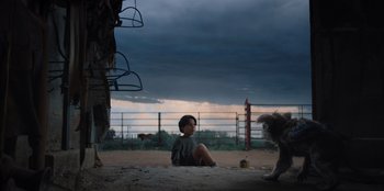 Movie still from “Chupa” (2023), directed by Jonás Cuarón – A person sitting on the ground next to a dog; Wide shot, Low angle