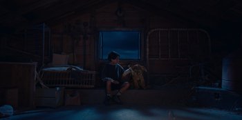 Movie still from “Chupa” (2023), directed by Jonás Cuarón – A person sitting on the steps of a house with a horse; Wide shot, Low angle