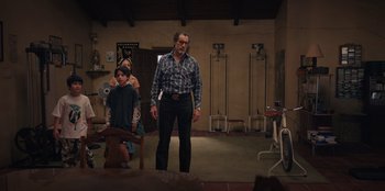 Movie still from “Chupa” (2023), directed by Jonás Cuarón – A group of people in a room with a man standing in front of a woman; Wide shot, Low angle