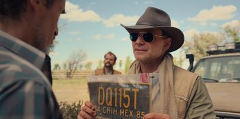 Movie still from “Chupa” (2023), directed by Jonás Cuarón – A man in a hat and sunglasses holding a license plate; Close Up shot, Over the shoulder angle
