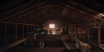 Movie still from “Chupa” (2023), directed by Jonás Cuarón – An attic room with boxes and a person sitting on the floor; Extreme Wide shot, Low angle