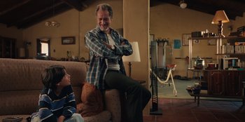 Movie still from “Chupa” (2023), directed by Jonás Cuarón – A man sitting on top of a couch next to a boy; Medium shot, Over the shoulder angle