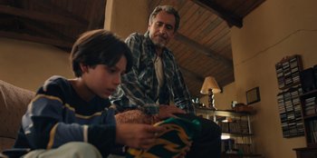 Movie still from “Chupa” (2023), directed by Jonás Cuarón – An older man and a young boy sitting on a couch; Medium shot, Over the shoulder angle