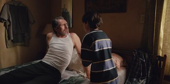 Movie still from “Chupa” (2023), directed by Jonás Cuarón – An older man talking to a young boy in a bedroom; Medium shot, Over the shoulder angle