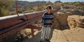 Movie still from “Chupa” (2023), directed by Jonás Cuarón – A young boy standing on top of a dirt hill; Wide shot, High angle