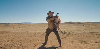 Movie still from “Chupa” (2023), directed by Jonás Cuarón – A man holding a dog in his arms in the desert; Wide shot, Low angle