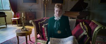 Movie still from “Cinderella” (2021), directed by Kay Cannon – A woman sitting on a chair holding a map; Medium shot, Low angle