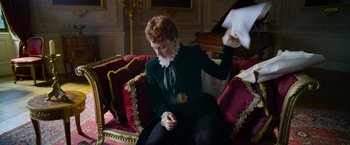 Movie still from “Cinderella” (2021), directed by Kay Cannon – A woman sitting on top of a red couch; Medium shot, Low angle