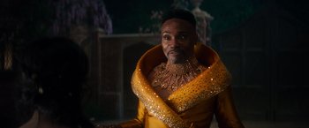 Movie still from “Cinderella” (2021), directed by Kay Cannon – A man in a yellow outfit and a gold necklace; Close Up shot, Over the shoulder angle