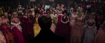 Movie still from “Cinderella” (2021), directed by Kay Cannon – A group of people in a room with a man standing in front of them; Wide shot, Over the shoulder angle