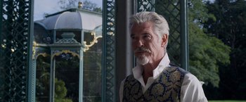 Movie still from “Cinderella” (2021), directed by Kay Cannon – An older man with white hair wearing a vest; Close Up shot, Over the shoulder angle