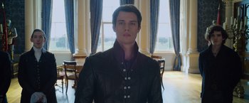 Movie still from “Cinderella” (2021), directed by Kay Cannon – A man in a black jacket standing in front of a window; Medium shot, Low angle