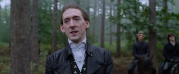 Movie still from “Cinderella” (2021), directed by Kay Cannon – A man in a black jacket standing in the woods; Close Up shot, Low angle