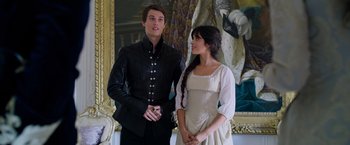 Movie still from “Cinderella” (2021), directed by Kay Cannon – A man and a woman standing next to each other in front of a painting; Medium shot, Low angle