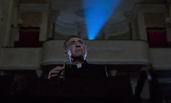 Movie still from “Cinema Paradiso” (1988), directed by Giuseppe Tornatore – A man in a priest's outfit holding a glass of wine; Medium shot, Low angle