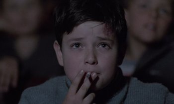 Movie still from “Cinema Paradiso” (1988), directed by Giuseppe Tornatore – A young boy is sitting in front of a projector screen; Close Up shot, High angle