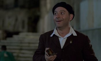 Movie still from “Cinema Paradiso” (1988), directed by Giuseppe Tornatore – A man in a brown jacket and a black hat holding something; Medium shot, Low angle