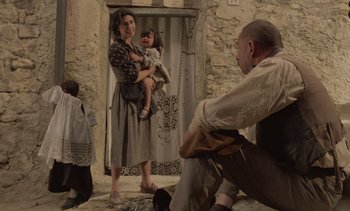 Movie still from “Cinema Paradiso” (1988), directed by Giuseppe Tornatore – A woman holding a child and a man kneeling down; Wide shot, Over the shoulder angle