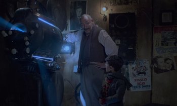 Movie still from “Cinema Paradiso” (1988), directed by Giuseppe Tornatore – A man and a boy standing in front of an old movie projector; Medium shot, Low angle